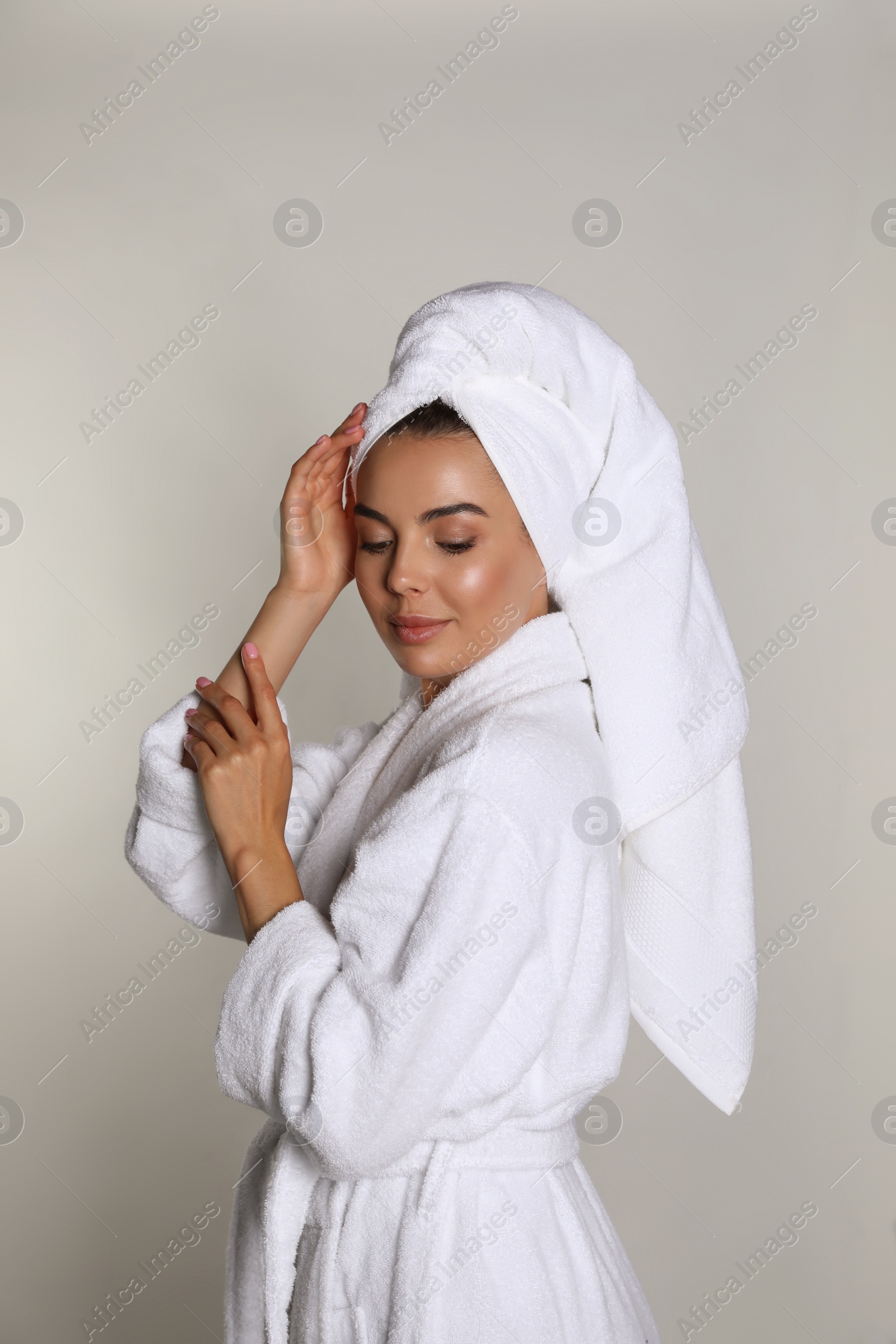 Photo of Beautiful young woman wearing bathrobe and towel on head against light background