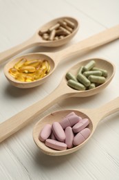 Photo of Different vitamin capsules in spoons on white wooden table, closeup