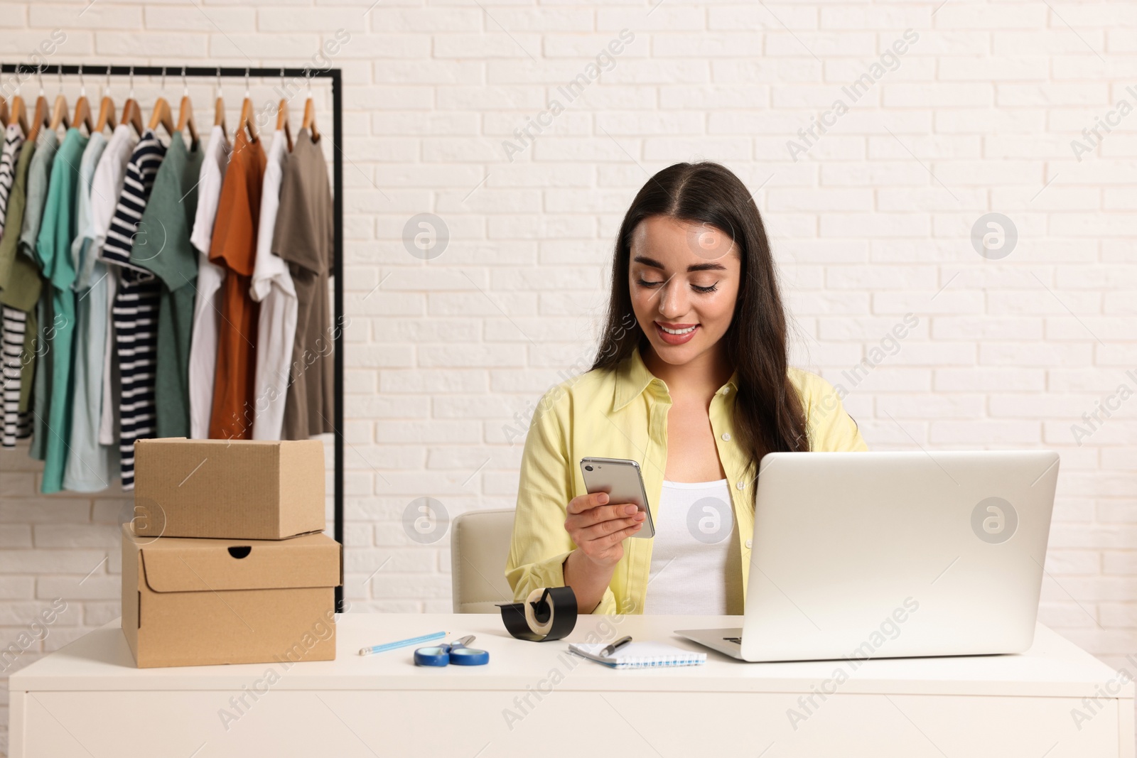 Photo of Seller with laptop and parcels using smartphone in office. Online store