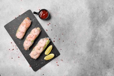 Photo of Tasty spring rolls served with spices, lime and sauce on grey textured table, flat lay. Space for text