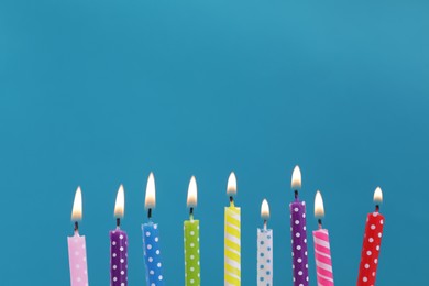 Photo of Many burning candles on light blue background, closeup. Birthday celebration