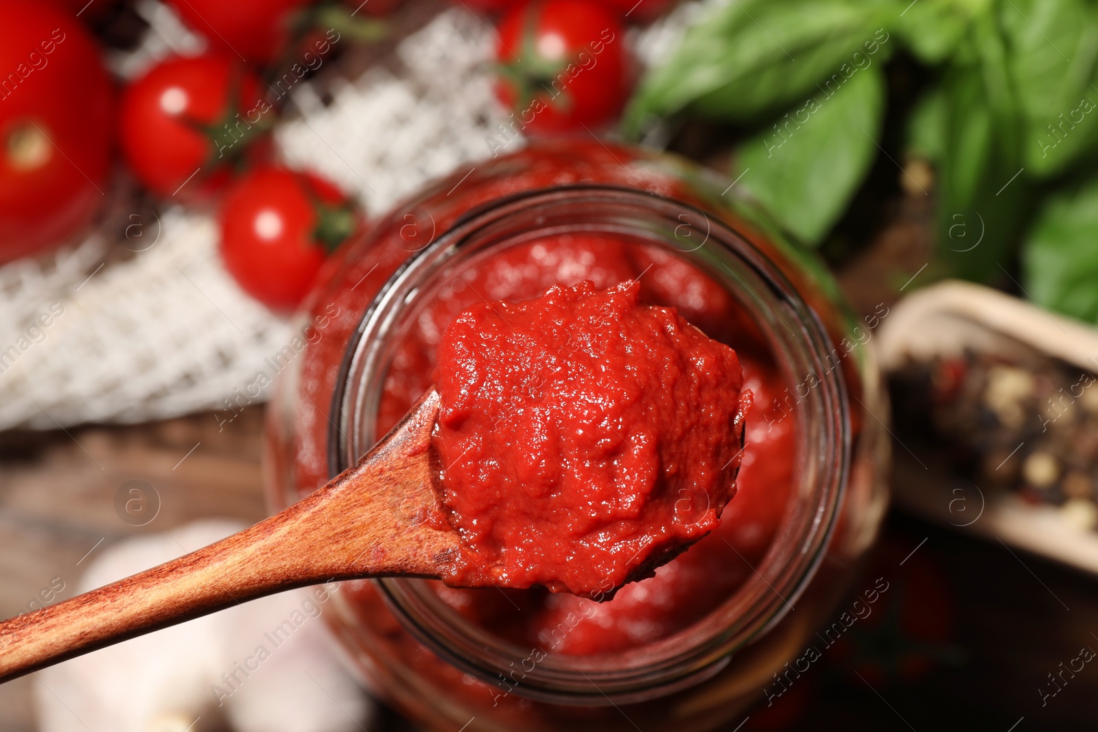 Photo of Taking tasty tomato sauce with wooden spoon from jar on table, top view