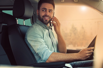 Image of Handsome young man talking on smartphone while driving his car