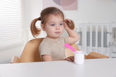 Photo of Cute little child eating tasty yogurt from plastic cup with spoon at white table indoors