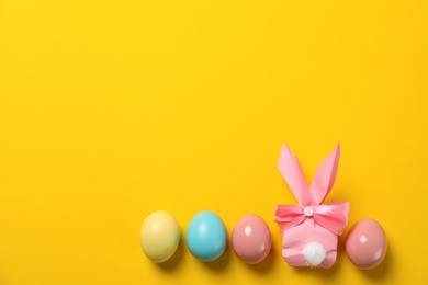 Photo of Flat lay composition of Easter bunny gift bag and dyed eggs on color background. Space for text