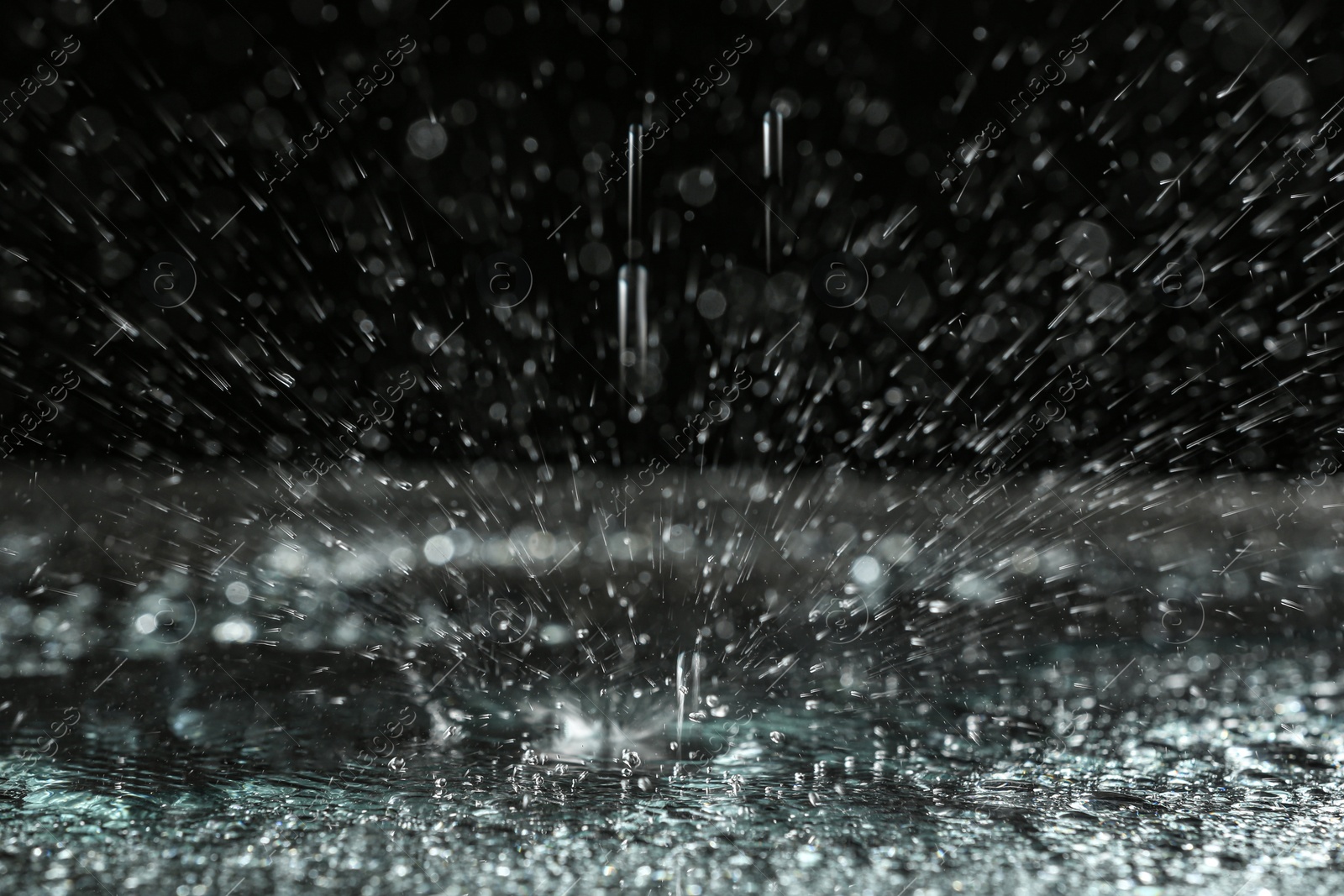 Photo of Rain drop falling down into puddle on dark background