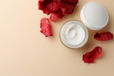 Jar of face cream and red flower petals on beige background, flat lay. Space for text