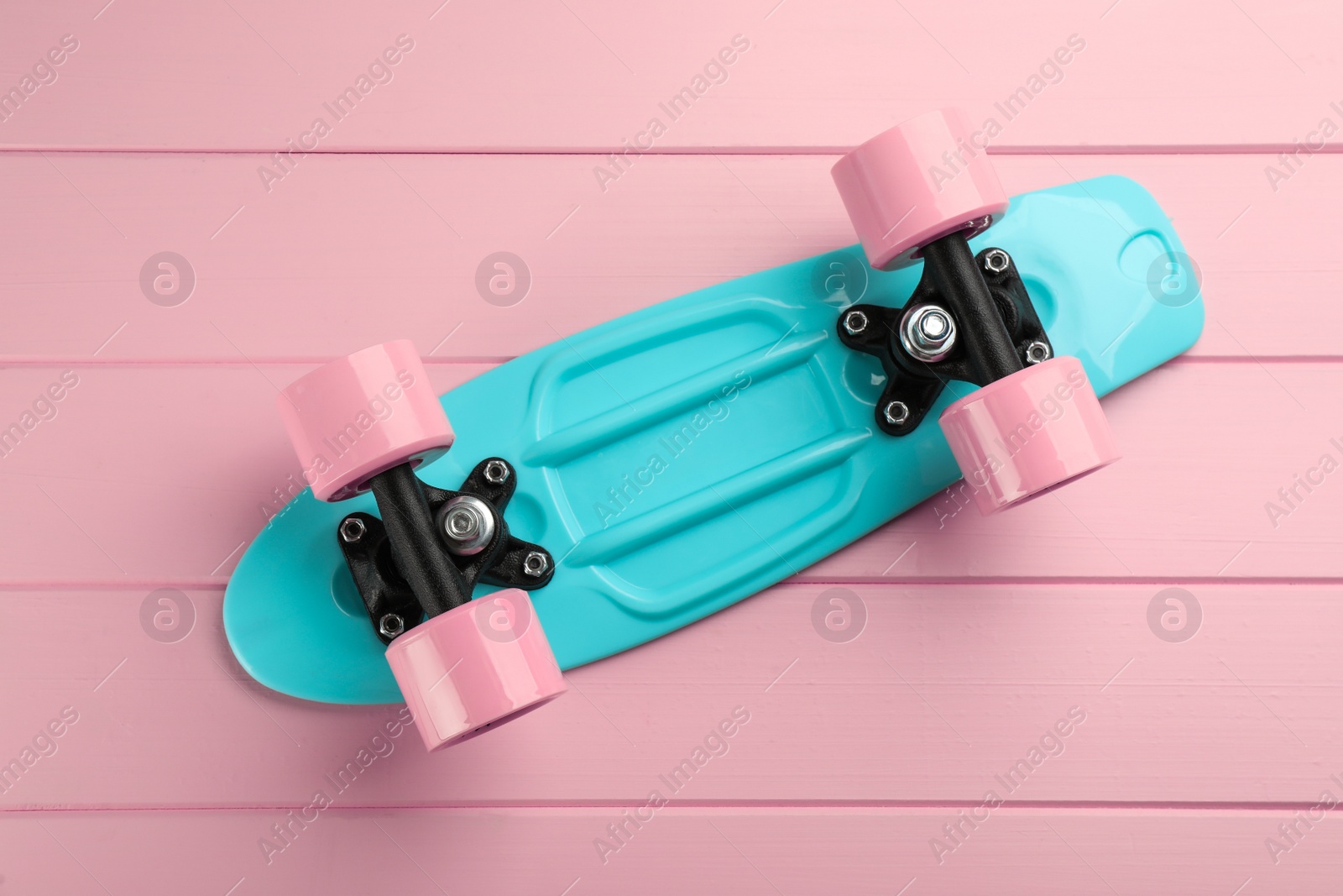 Photo of Turquoise skateboard on pink wooden background, top view. Sport equipment