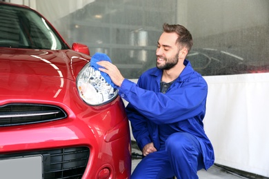 Photo of Worker cleaning automobile headlight with rag at car wash