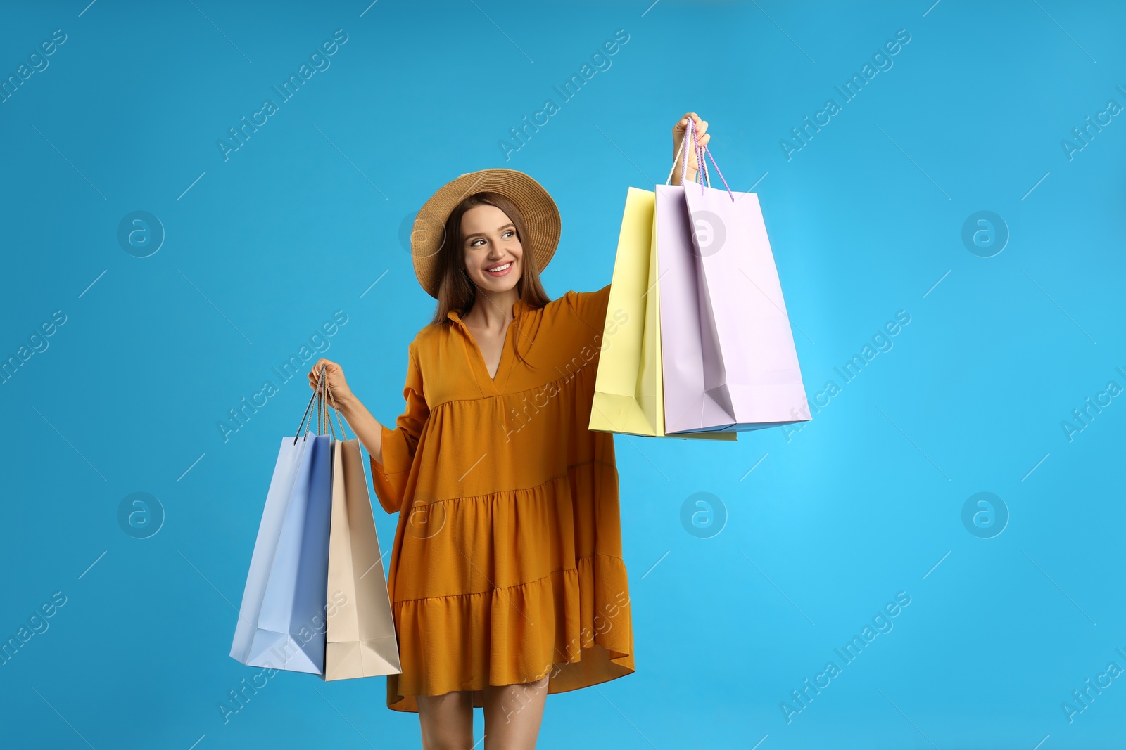 Photo of Beautiful young woman with paper shopping bags on light blue background