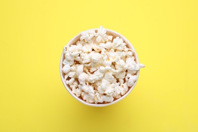 Photo of Paper bucket with delicious popcorn on yellow background, top view