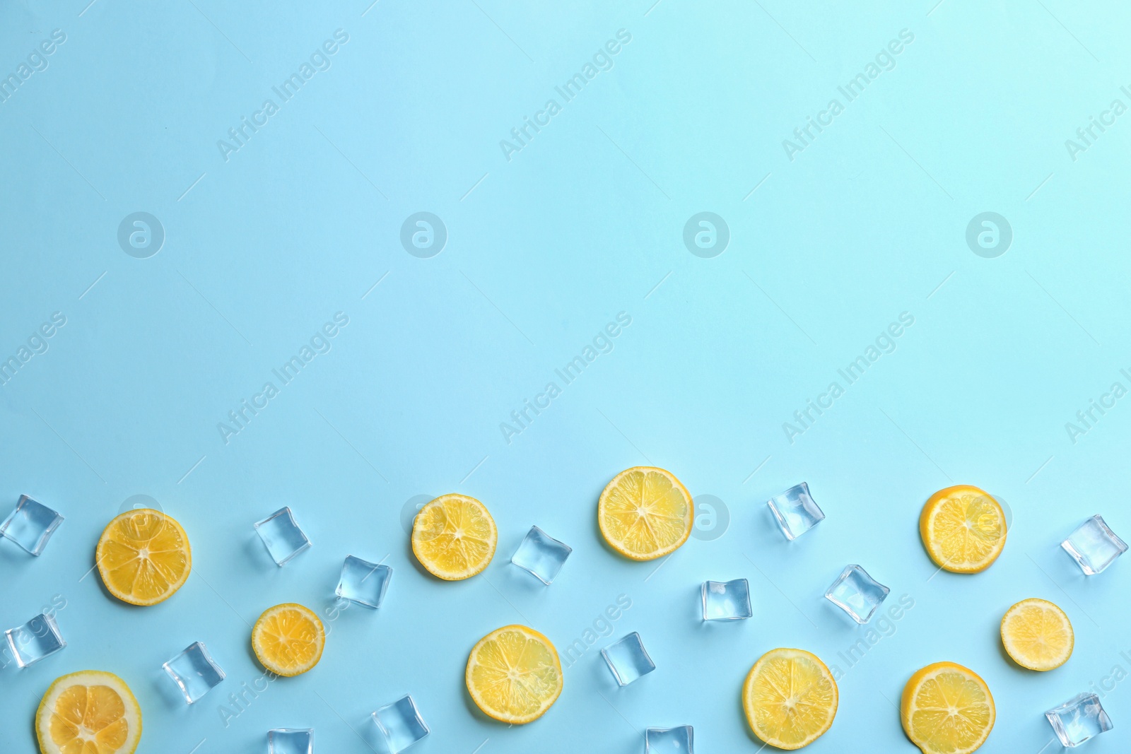 Photo of Lemonade layout with juicy lemon slices and ice cubes on light blue background, top view. Space for text