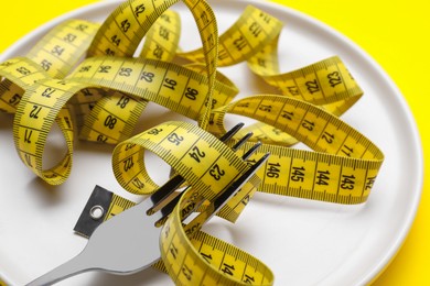 Photo of Measuring tape and fork on yellow background, closeup. Weight loss concept