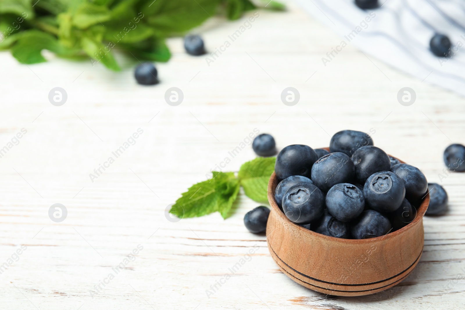 Photo of Wooden bowl with tasty blueberries on white table, space for text
