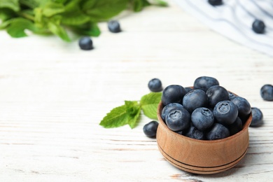 Wooden bowl with tasty blueberries on white table, space for text