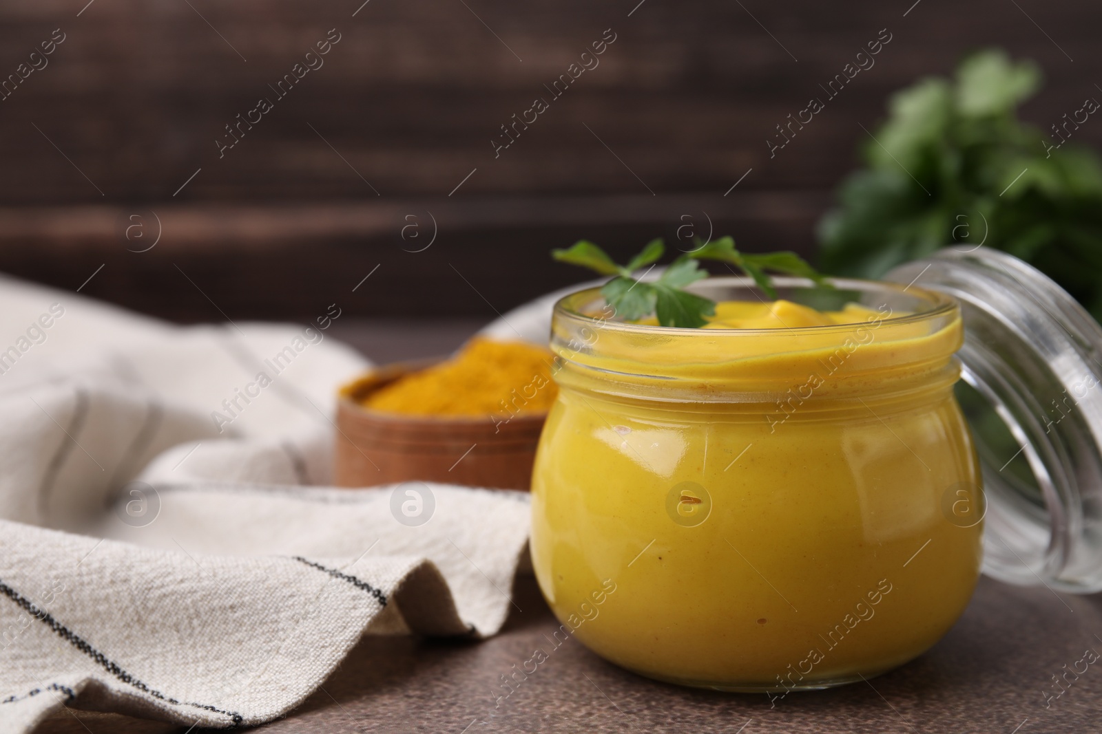 Photo of Jar with tasty curry sauce and parsley on brown table, closeup. Space for text