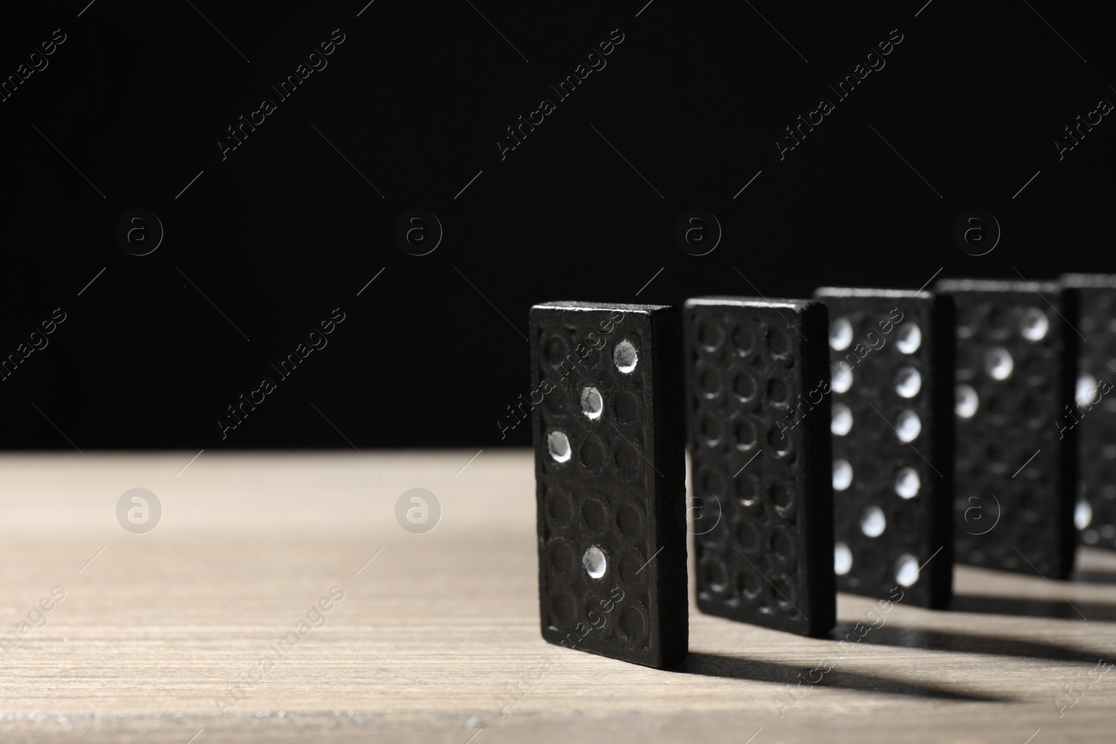 Photo of Domino tiles on wooden table against black background. Space for text