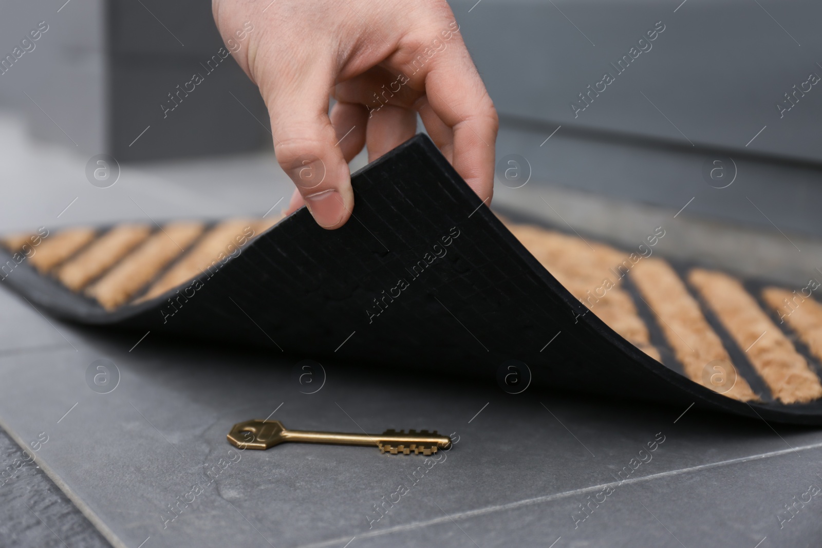 Photo of Man lifting door mat and finding hidden key, closeup view