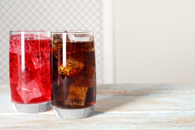 Glasses of different refreshing soda water with ice cubes on white wooden table, space for text