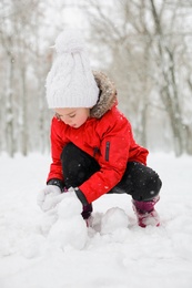 Photo of Cute little girl making snowballs outdoors on winter day