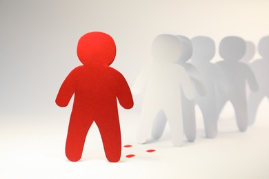 Photo of White paper human figures following red one on light background. Responsibility concept