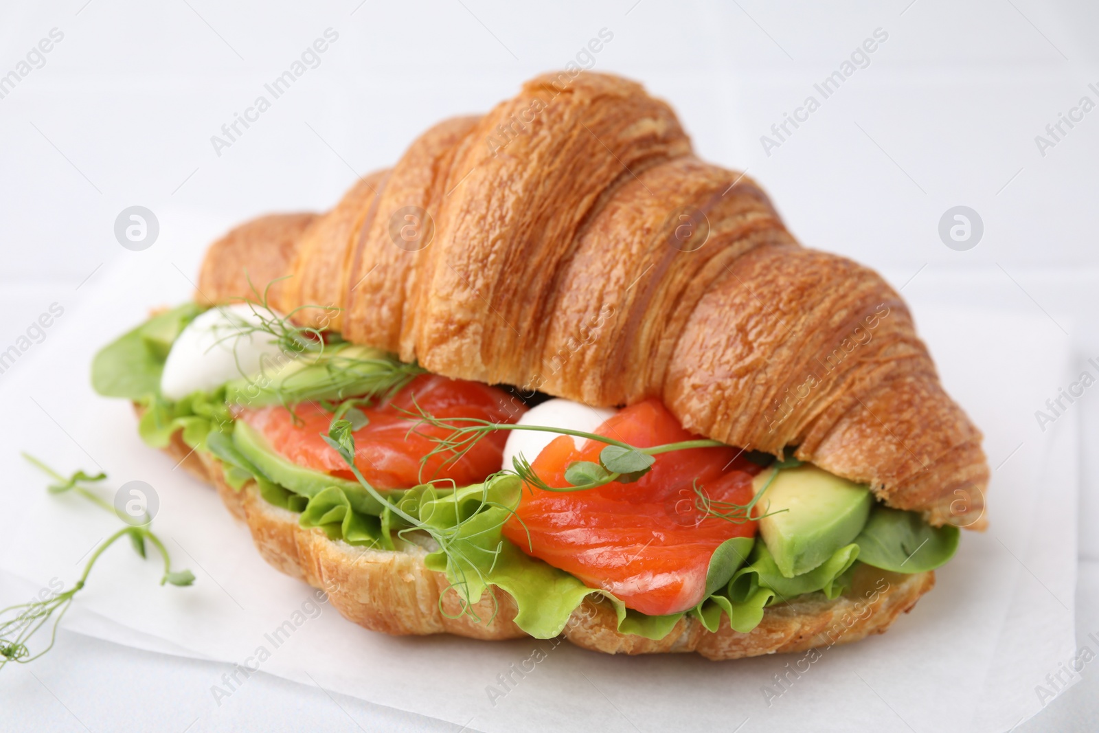 Photo of Tasty croissant with salmon, avocado, mozzarella and lettuce on white table, closeup
