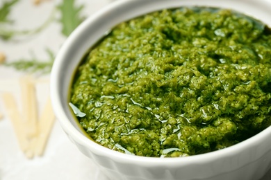 Photo of Bowl of tasty arugula pesto on table, closeup