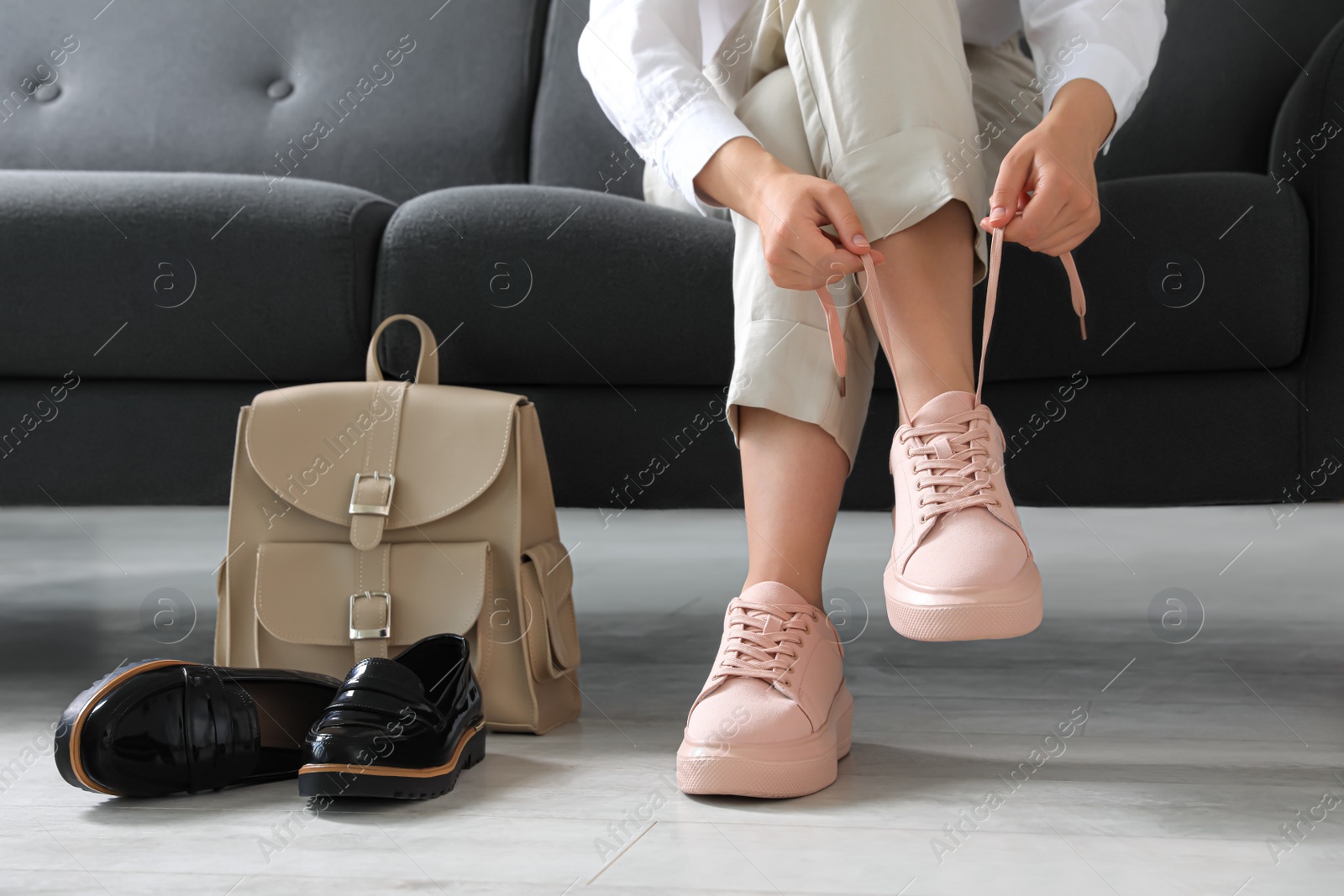 Photo of Woman taking off uncomfortable shoes and putting on sneakers in office, closeup