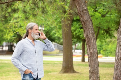 Photo of Handsome mature man with mobile phone in green park