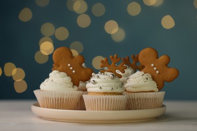 Photo of Tasty Christmas cupcakes on white wooden table against blurred festive lights