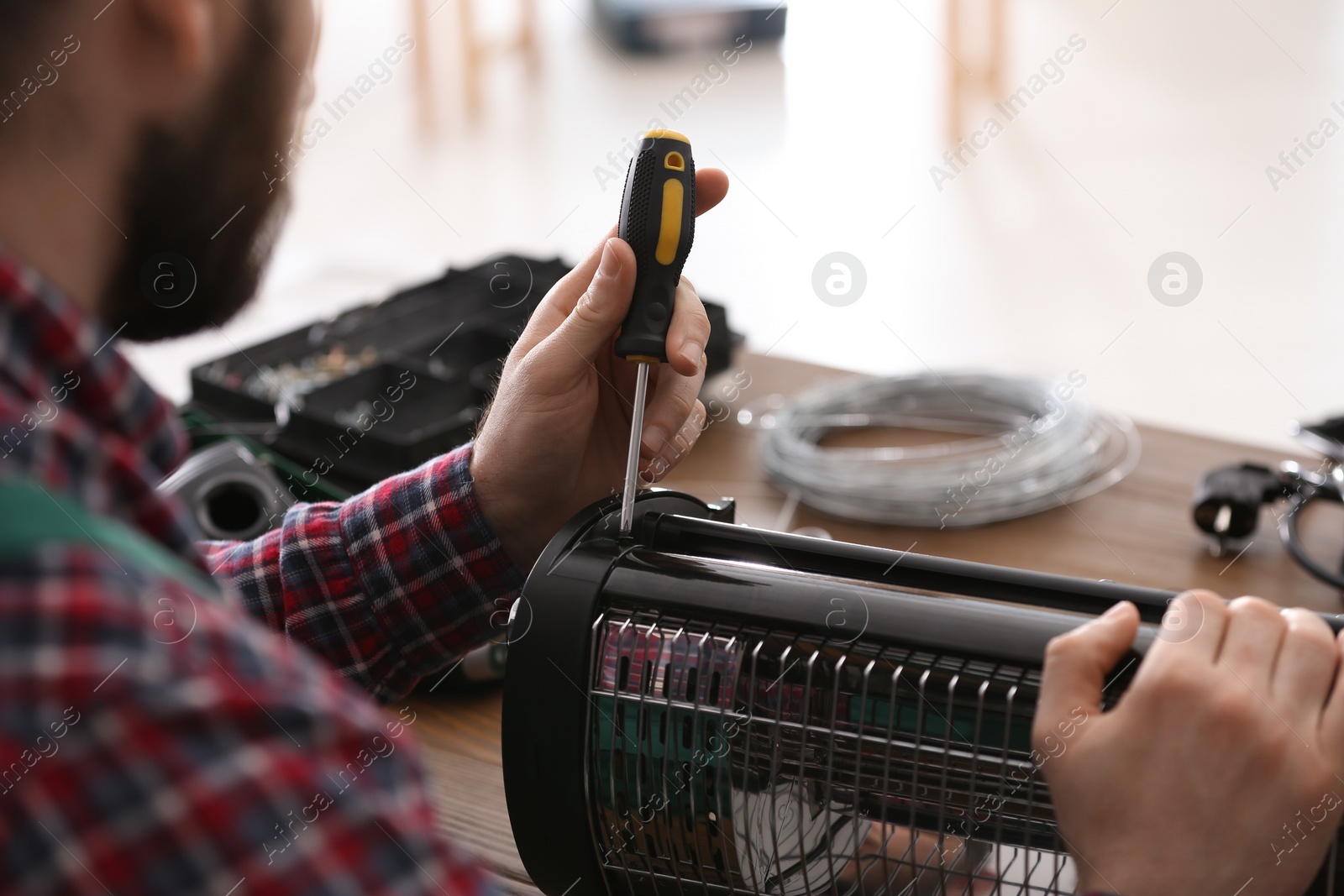 Photo of Professional technician repairing electric halogen heater with screwdriver at table indoors, closeup