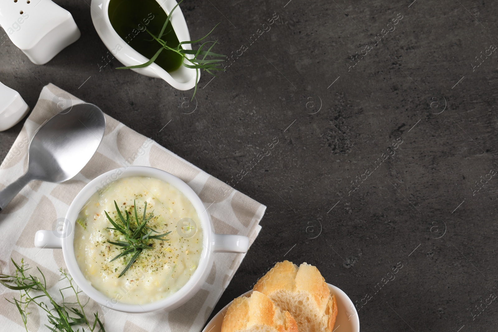 Photo of Delicious cream soup with tarragon, spices and potato in bowl served on dark textured table, flat lay. Space for text