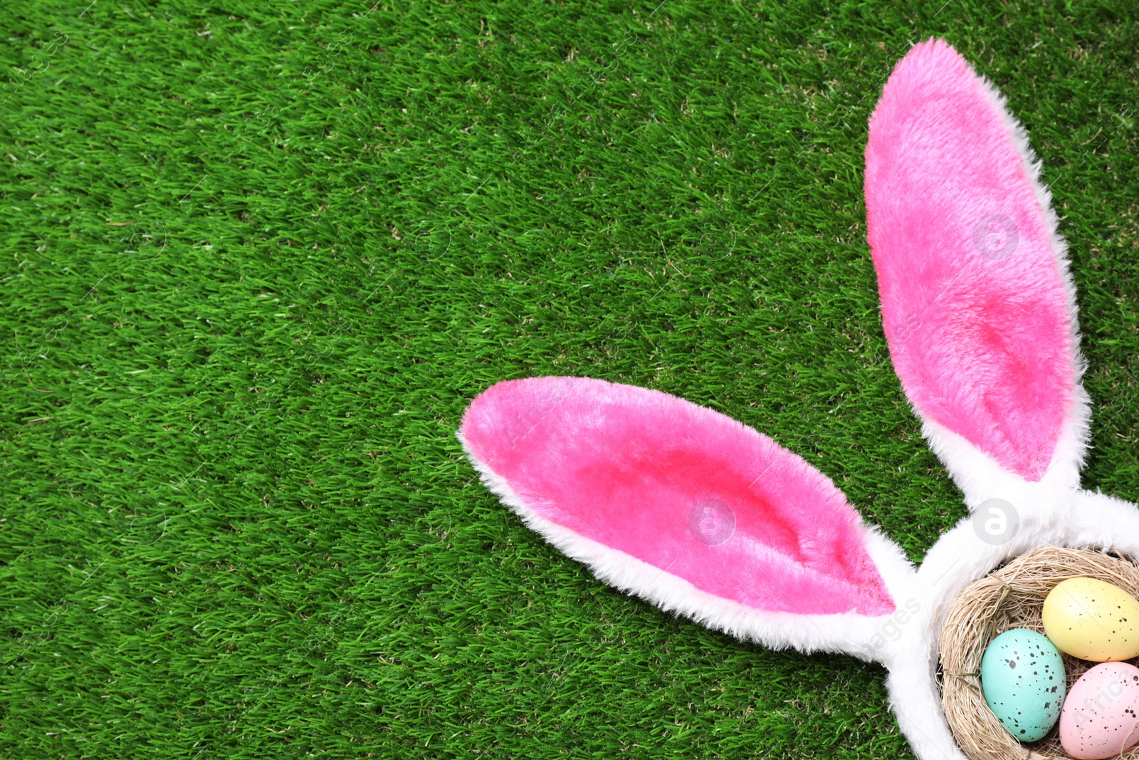 Photo of Headband with bunny ears, painted eggs and space for text on grass, flat lay. Easter holiday