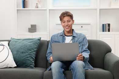 Happy young man having video chat via laptop on sofa indoors