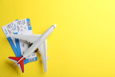 Toy airplane and tickets on yellow background, flat lay. Space for text