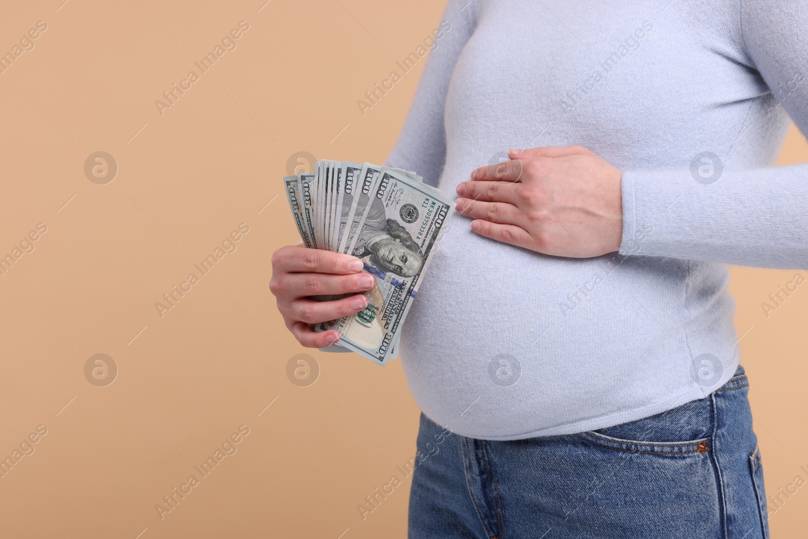 Photo of Surrogate mother. Pregnant woman with dollar banknotes on beige background, closeup. Space for text