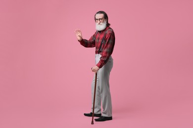 Photo of Senior man with walking cane waving on pink background