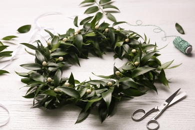 Photo of Beautiful handmade mistletoe wreath and florist supplies on white wooden table. Traditional Christmas decor