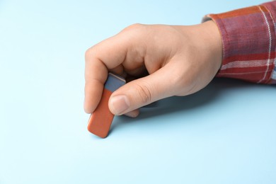 Photo of Man erasing something on light blue background, closeup