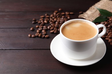 Cup of hot aromatic coffee and roasted beans on wooden table. Space for text