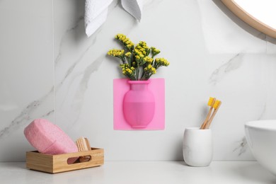 Silicone vase with flowers on white marble wall over countertop in stylish bathroom