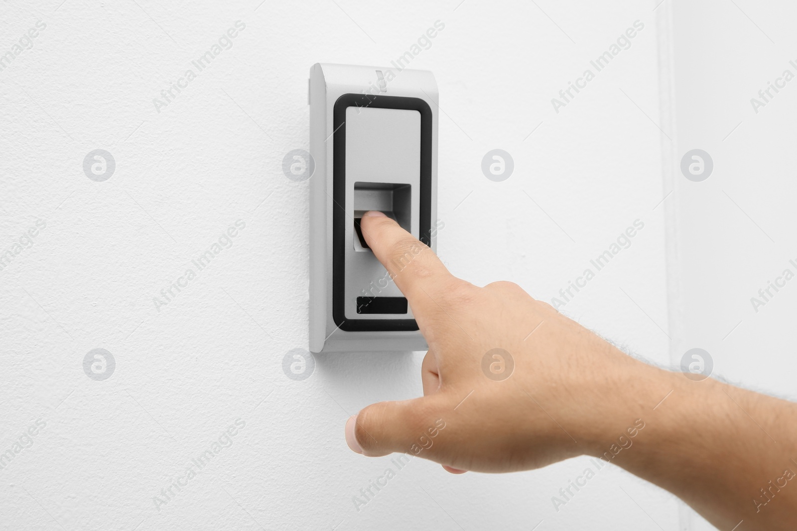 Photo of Young man pressing fingerprint scanner on alarm system indoors