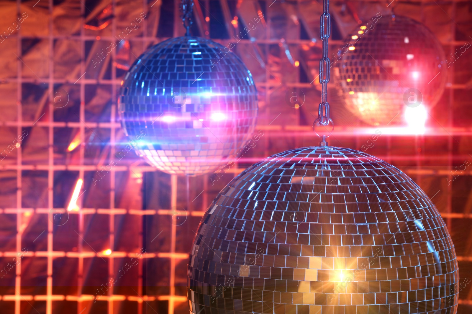 Photo of Shiny disco balls against foil party curtain under color lights