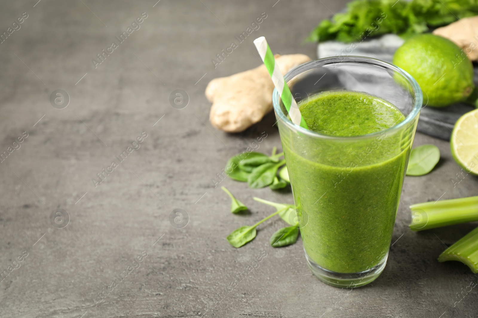 Photo of Green juice and fresh ingredients on grey table. Space for text