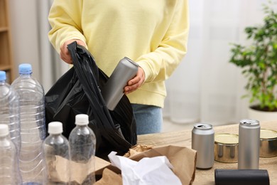 Photo of Woman separating garbage at table in room, closeup