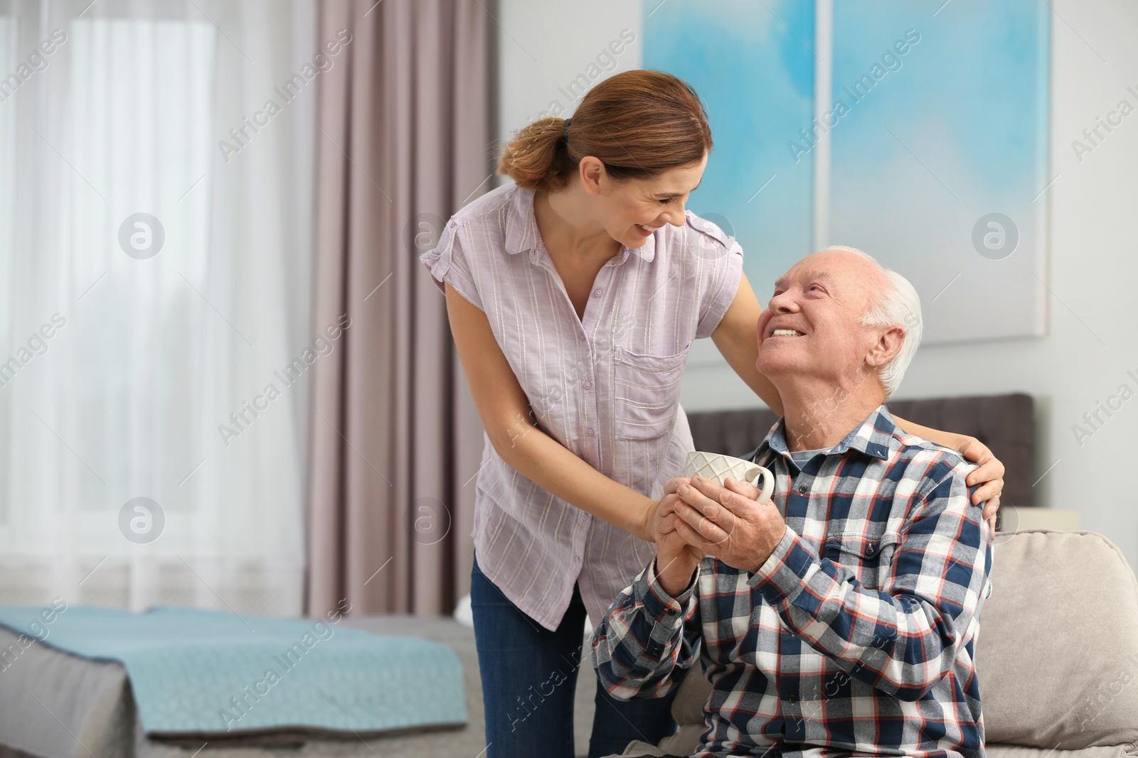 Photo of Elderly man with cup of tea near female caregiver at home. Space for text