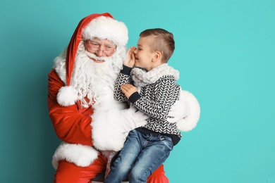 Photo of Little boy whispering in authentic Santa Claus' ear on color background