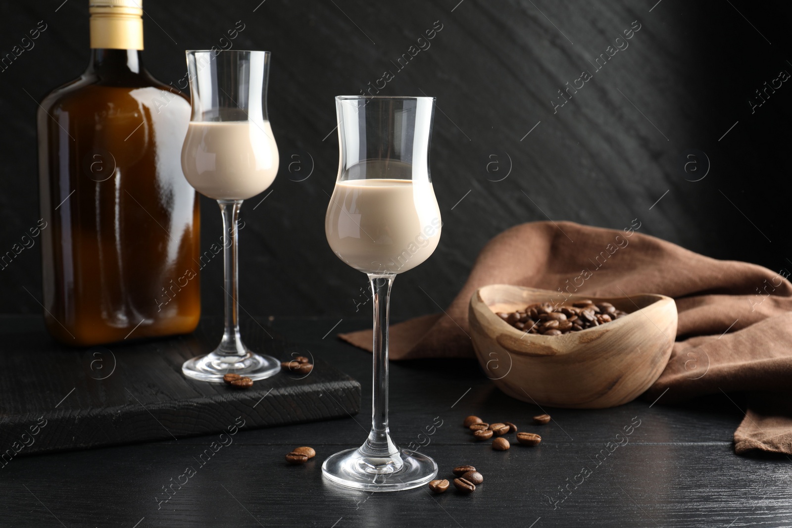 Photo of Coffee cream liqueur in glasses, bottle and beans on black wooden table