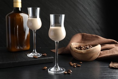 Coffee cream liqueur in glasses, bottle and beans on black wooden table