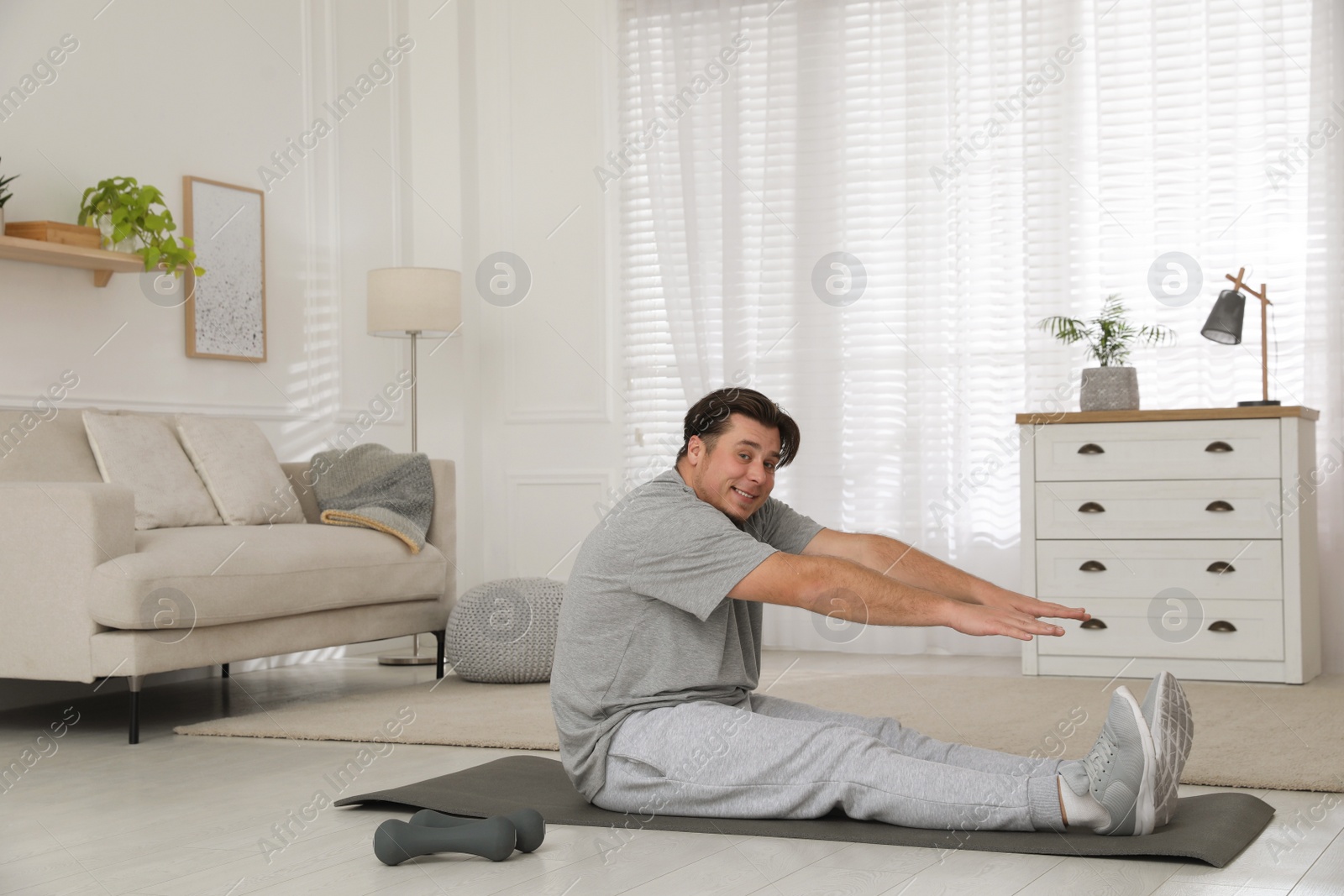 Photo of Overweight man stretching on mat at home, space for text